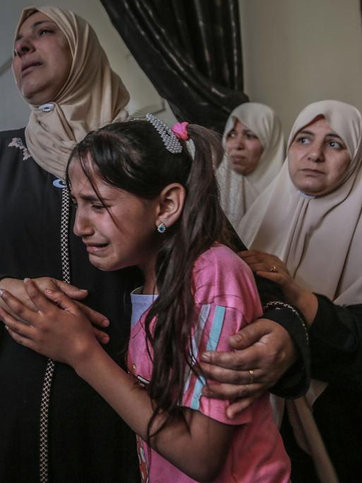 Angehörige trauern während einer Bestattungszeremonie eines bei einem israelischen Luftangriff getöteten Palästinensers. Zu sehen ist ein weinendes Mädchen und mehrere Frauen um sie herum.