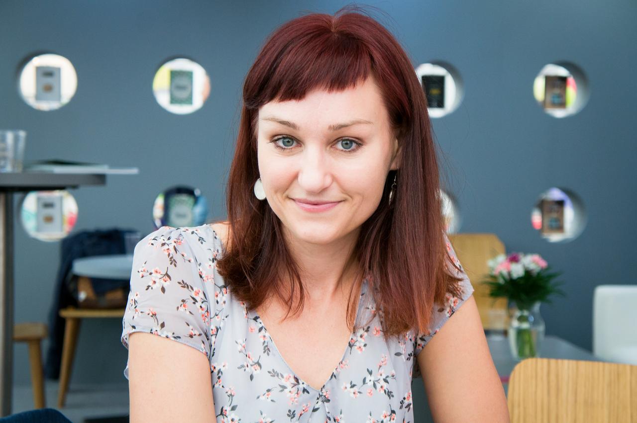 Kateřina Tučková lächelt in die Kamera. Eine junge Frau mit roten Haaren und assymmetrisch geschnittenem Pony.