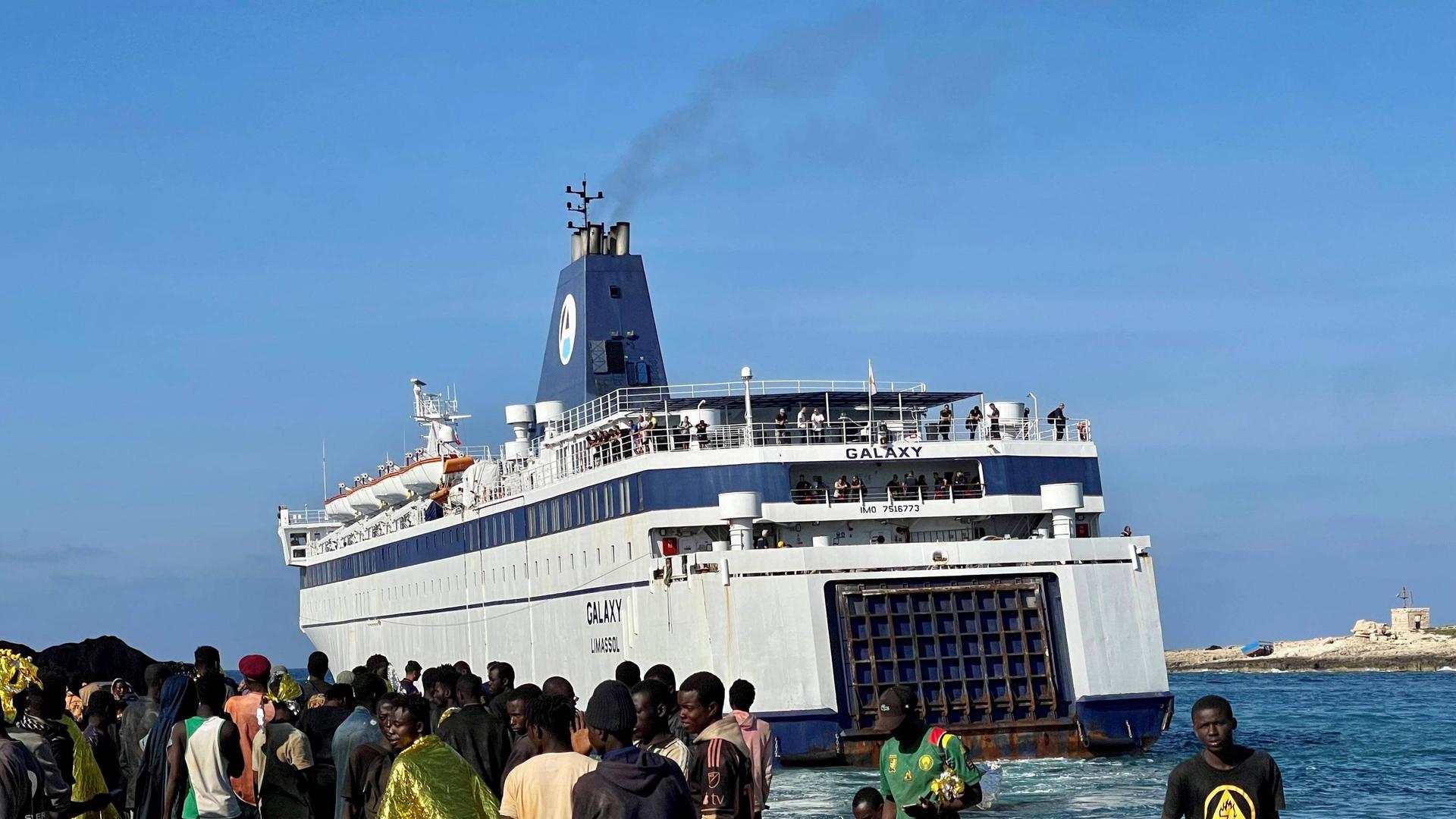 Migranten am Hafen von Lampedusa, Italien. Schiff im Hintergrund.