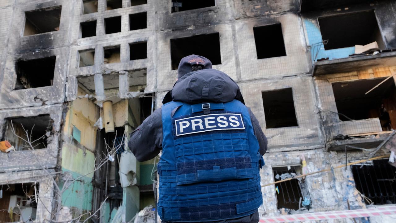 Das Bild zeigt einen Pressevertreter mit einer blauen Weste auf der "Press" in Englisch steht vor einem zerbombten Haus in Kyiv in der Ukraine im Jahr 2022.