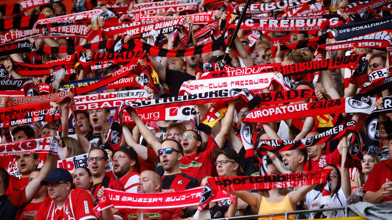 Fans des SC Freiburg halten ihre Schals in die Höhe. Szene aus dem Spiel gegen Augsburg am 01.10.2023.