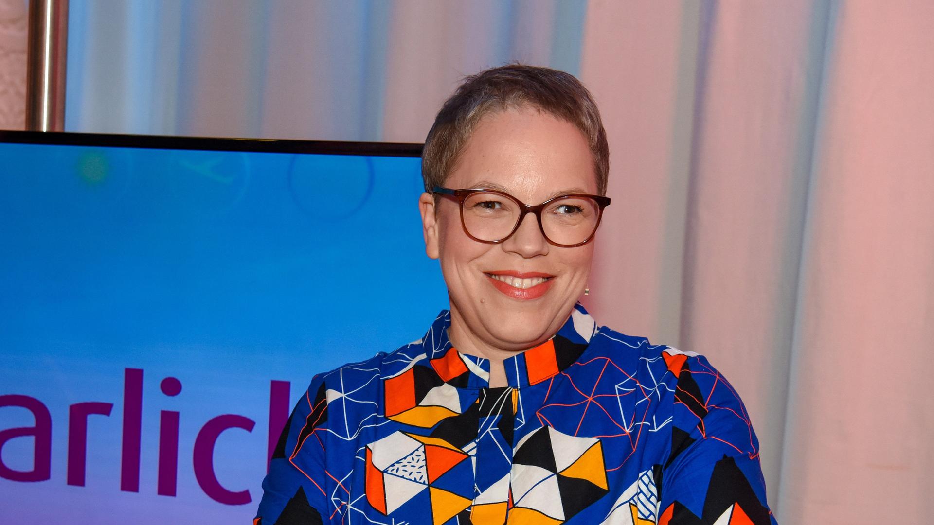 Die Journalistin und Kochbuch-Autorin Katharina Seiser im Jahr 2021 in der Kulisse von "Die Barbara Karlich Show". Sie trägt ein blau-bunt gemustertes Hemd.