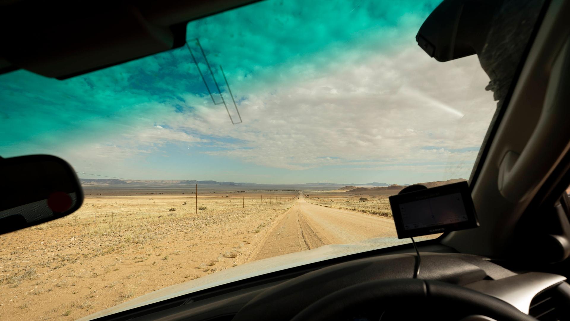 Blick durch die Scheibe eines Autos auf eine Sandpiste in der Wüste Namibias.