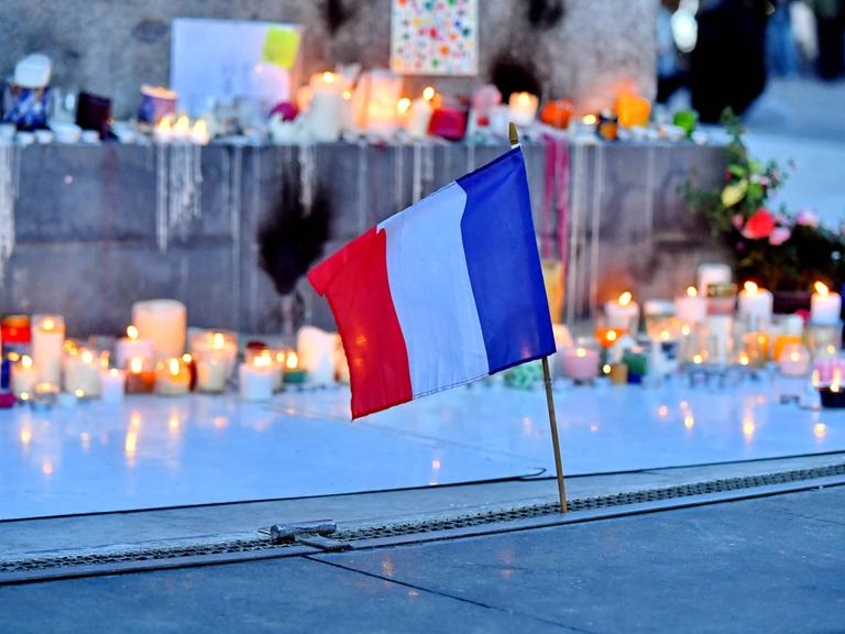 Anlässlich der Anschläge im Bataclan und der Terroranschläge auf die Terrassen der Pariser Cafés werden Kerzen aufgestellt und Blumen niedergelegt auf der Place de la République in Paris. Im Vordergrund ist eine kleine Frankreichfahne zu sehen 