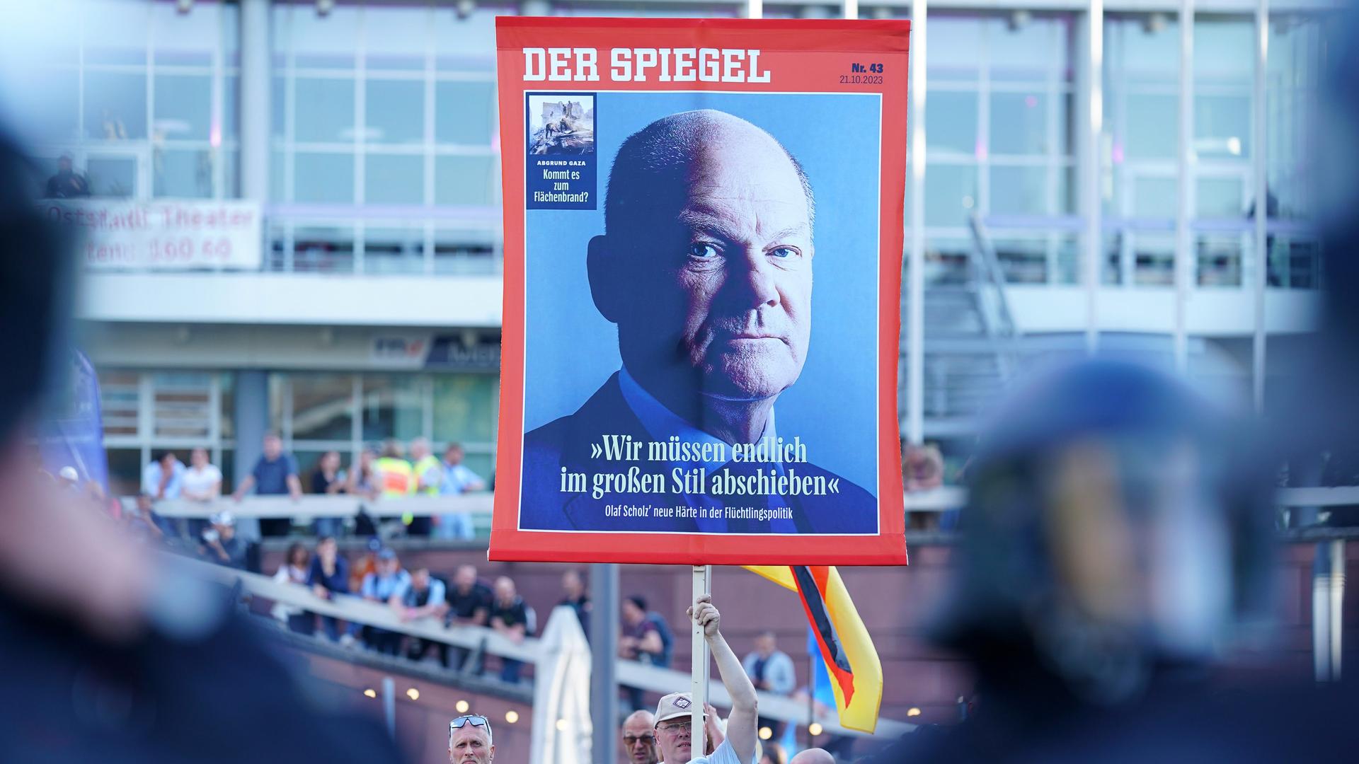 Ein Mann hält ein Plakat das einen Titel des Magazins "Der Spiegel" mit einem Bild von Bundeskanzler Olaf Scholz und der Aufschrift "Wir müssen endlich im großen Stil abschieben" zeigt.