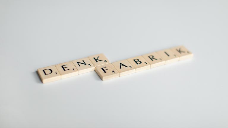 Scrabblesteine mit dem Wort Denkfabrik vor weißem Hintergrund