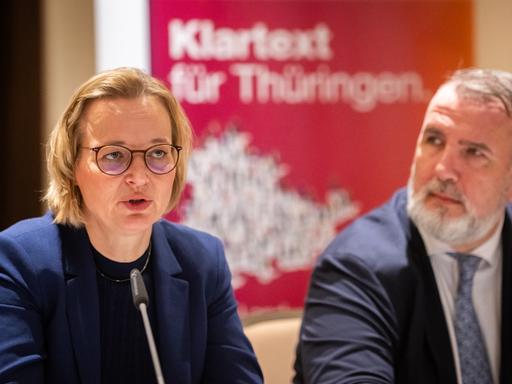 Auf dem Bild sieht man die Landesvositzenden des Bündnis Sahra Wagenknecht vor einem Mikrofon sitzen. Im Hintergrund erkennt man unscharf den Schriftzug "Klartext für Thüringen"