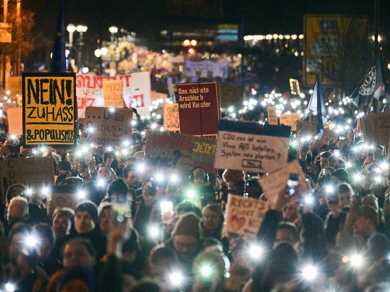 Eine Demonstration, die Menschen halten Schilder in die Höhe und haben das Licht ihrer Handys an. Es ist eine Kundgebung gegen die Zusammenarbeit der CDU mit der AfD. 