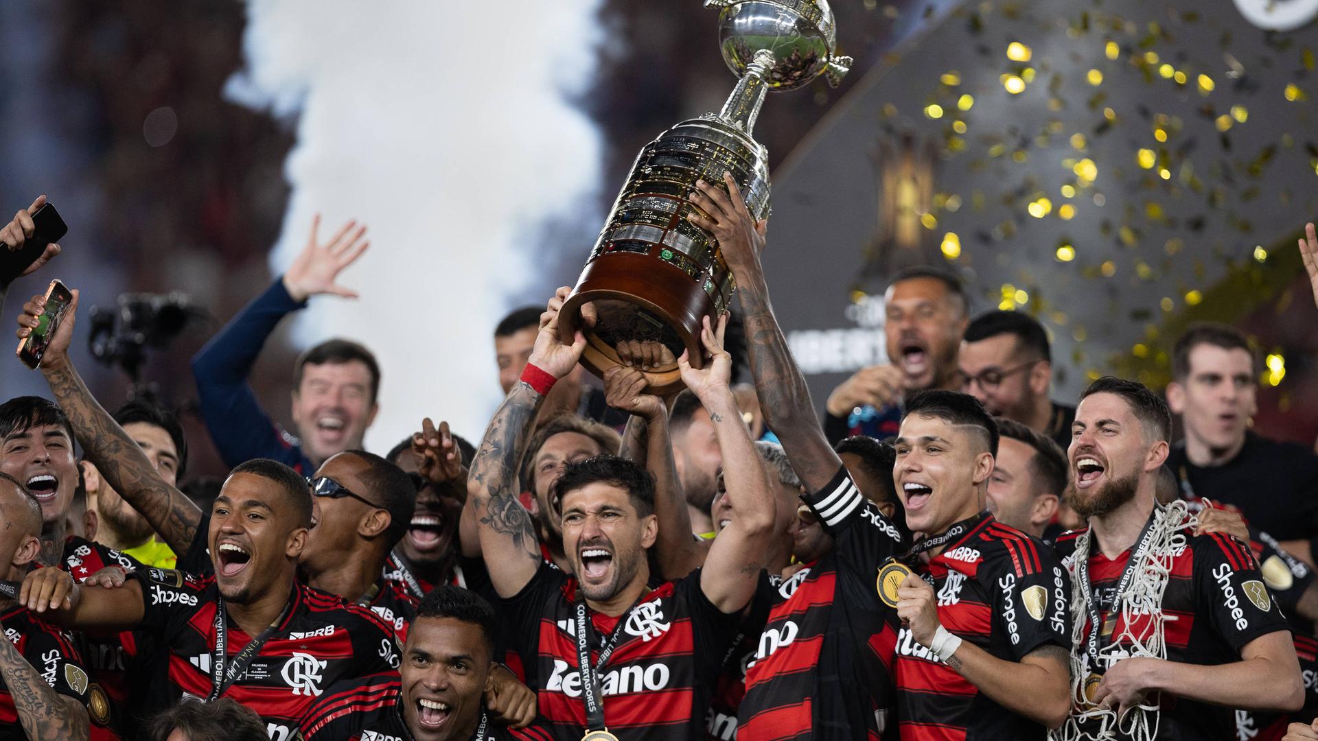 Die Spiele von Flamengo in schwarz-rot gestreiften Trikots stehen beieinander und jubeln über ihren Sieg, dabei halten sie den Pokal hoch.