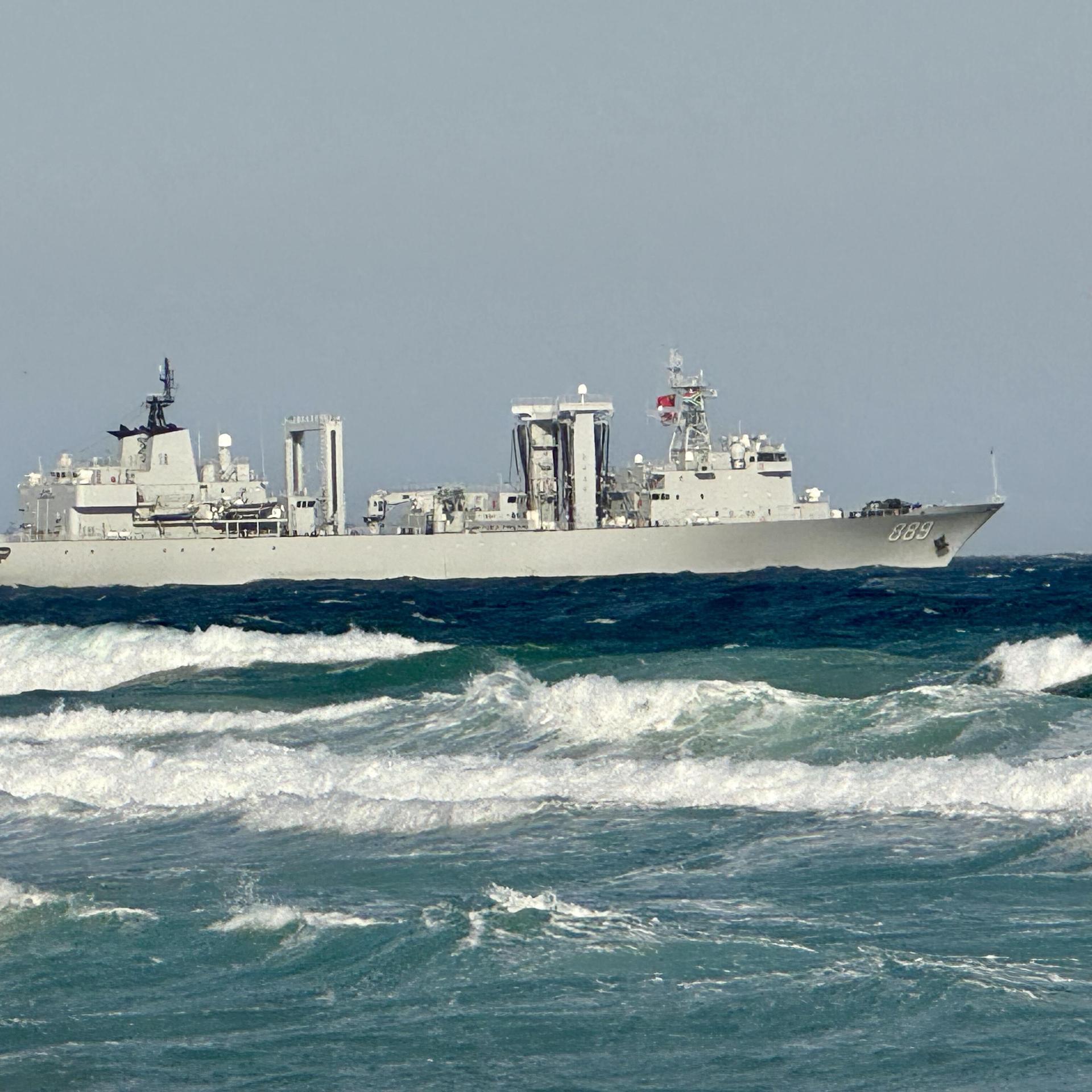 Ein Kriegsschiff kreuzt auf dem Wasser. Im Vordergrund sind starke Wellen zu sehen.