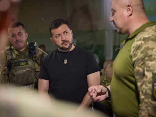 Ukraines Präsident Wolodymyr Selenskyj umringt von zwei Soldaten beim Truppenbesuch an der Front nahe von Saporischschja.