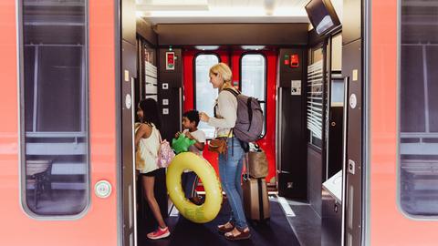 Eine Mutter und zwei Kinder mit Schwimmreifen und Wasserspielzeug steigen in eine Bahn ein.