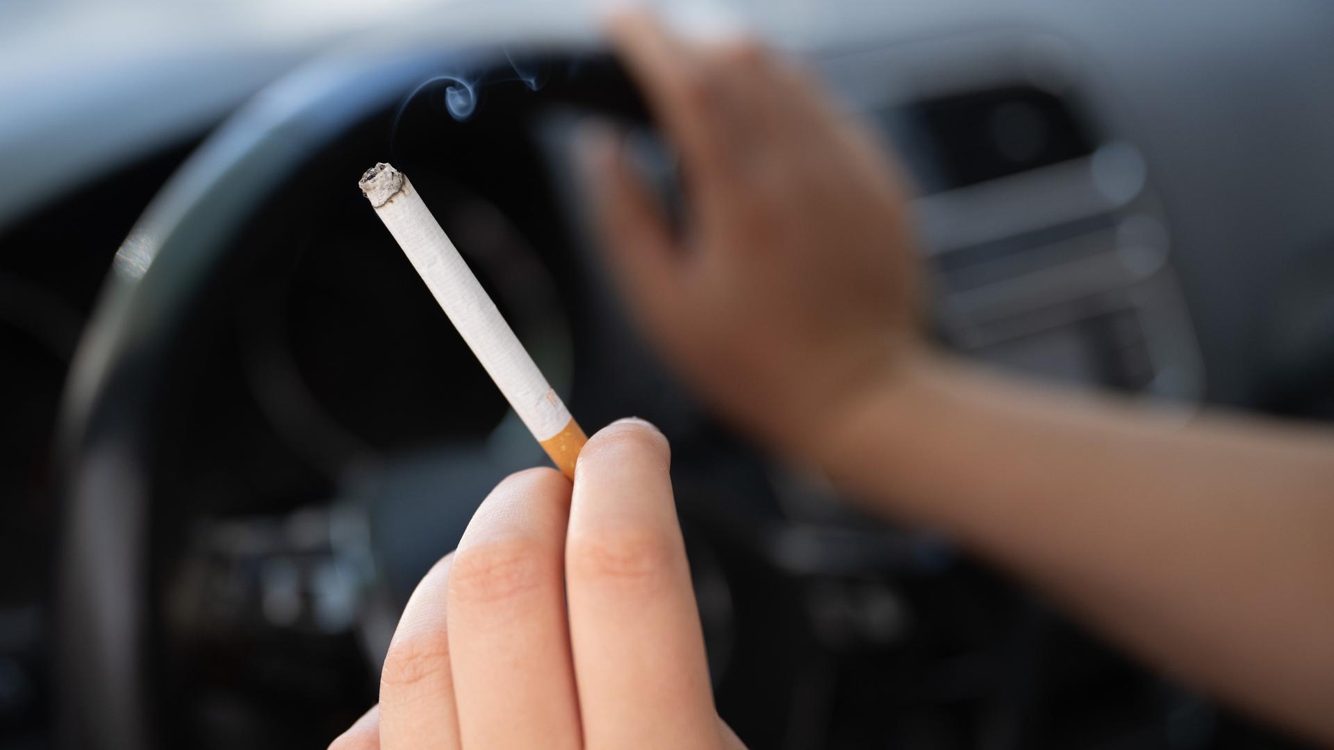 Eine Frau sitzt in einem PKW und hält eine Zigarette.