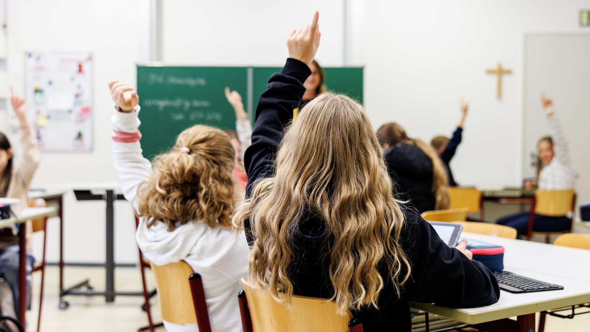 Zwei Mädchen sitzen im Klassenraum nebeneinander und melden sich.