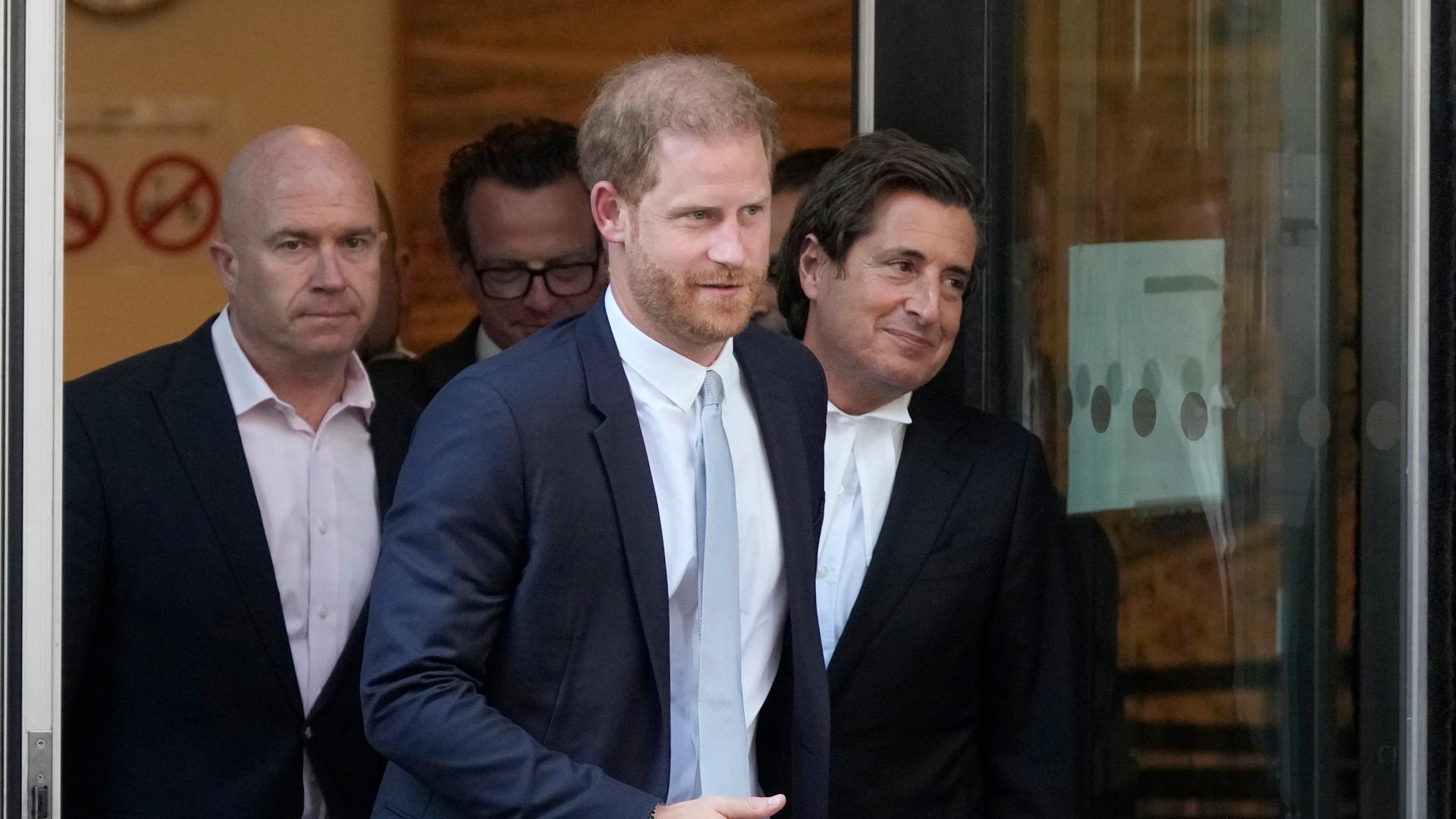 Prinz Harry tritt mit zwei Männern aus einem Gebäude.