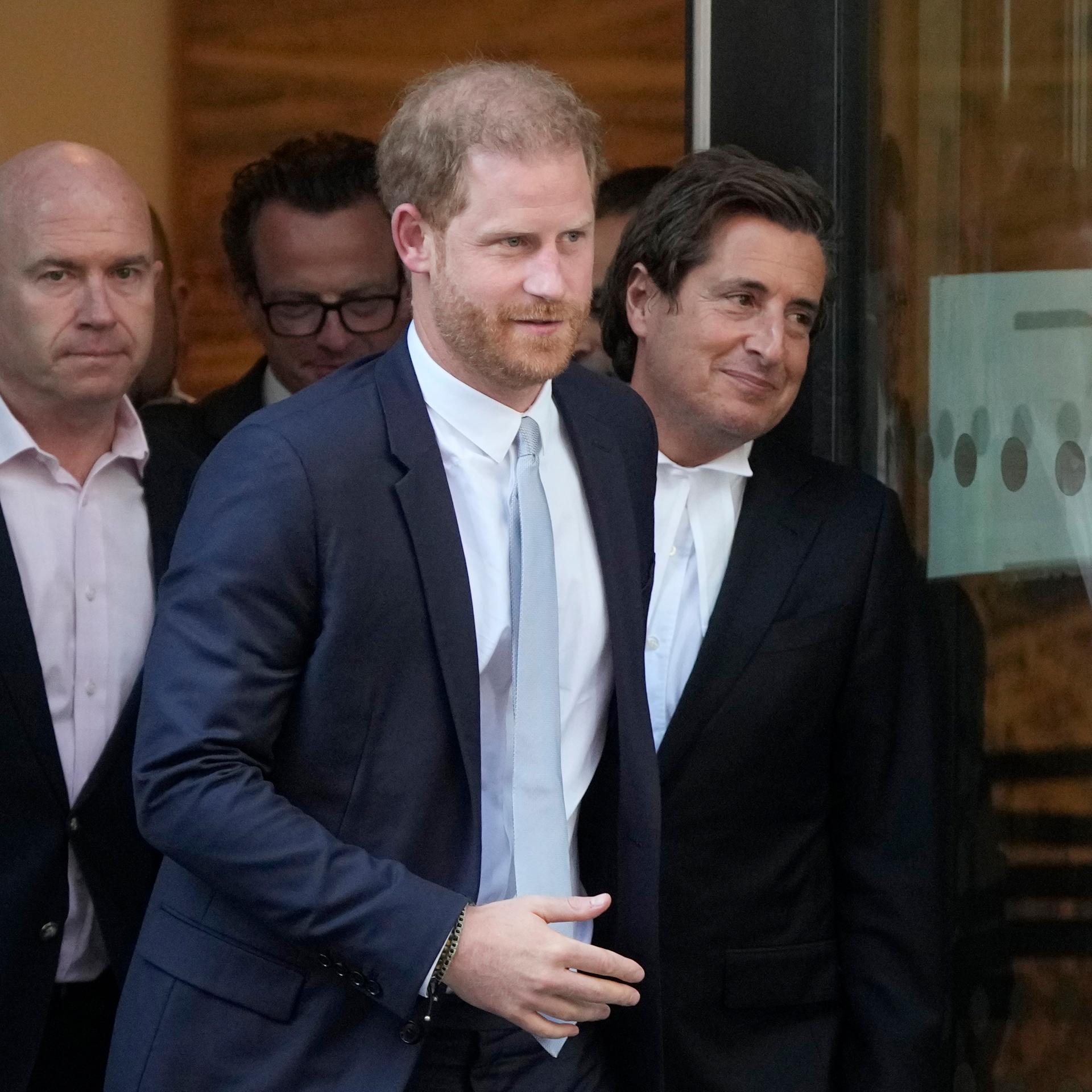 Prinz Harry tritt mit zwei Männern aus einem Gebäude.