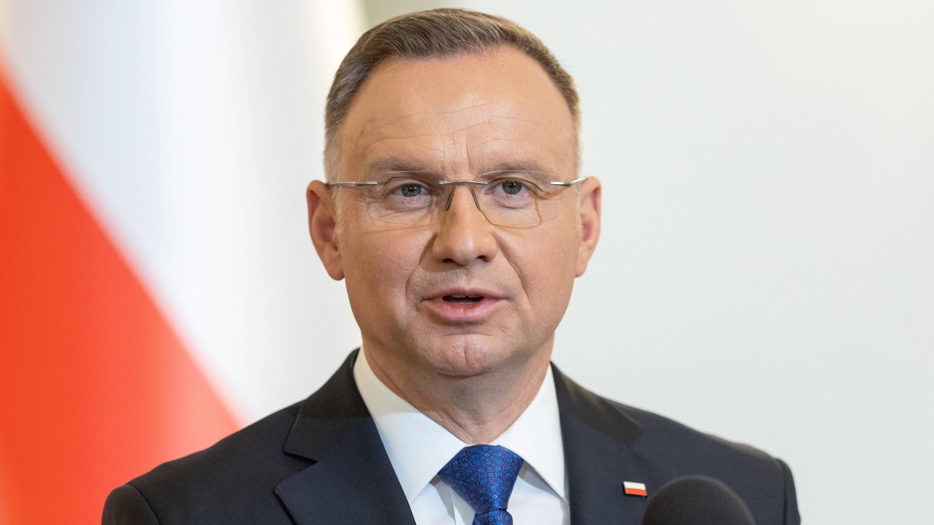 Polens Präsident Duda steht im Anzug vor einer polnischen Flagge an einem Rednerpult.
