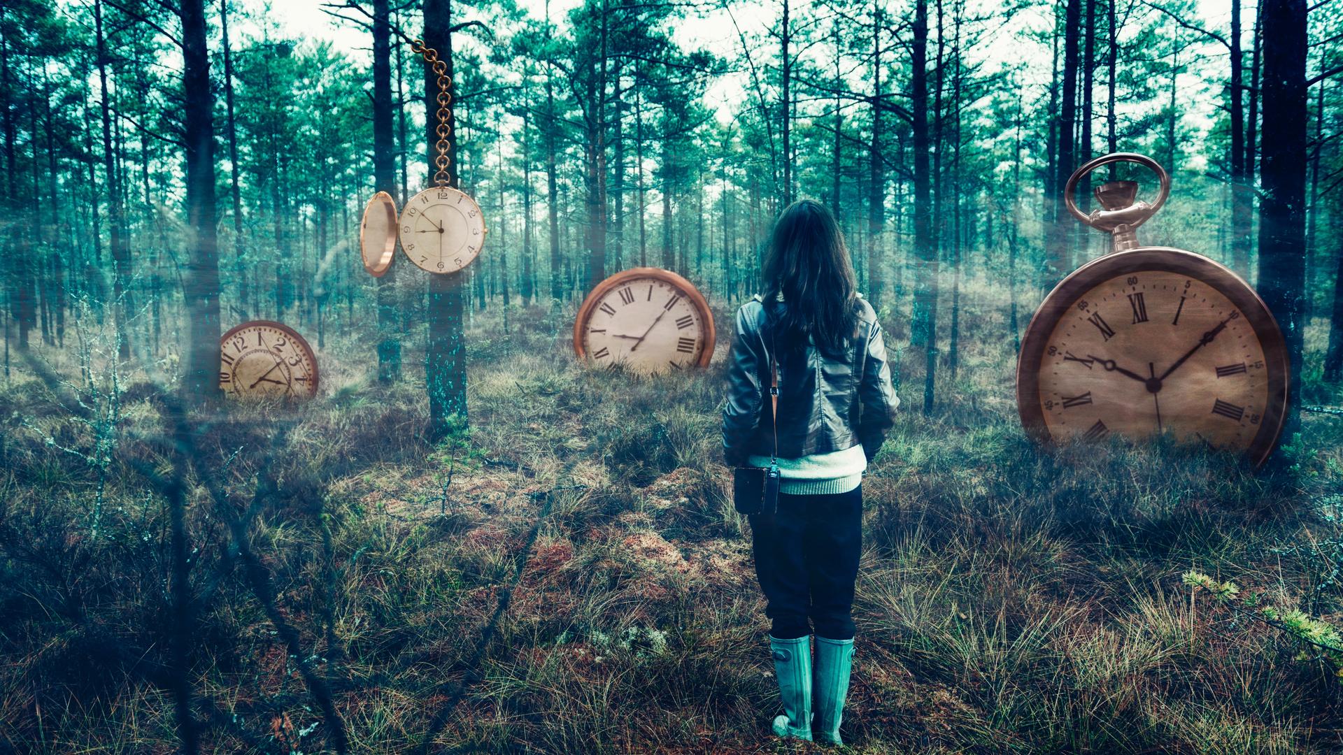 Eine Person steht mit dem Rücken zur Kamera in einem nebeligen Wald. Im Wald sind an den Bäumen und im Boden Uhren eingelassen.