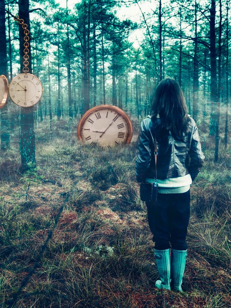 Eine Person steht mit dem Rücken zur Kamera in einem nebeligen Wald. Im Wald sind an den Bäumen und im Boden Uhren eingelassen.