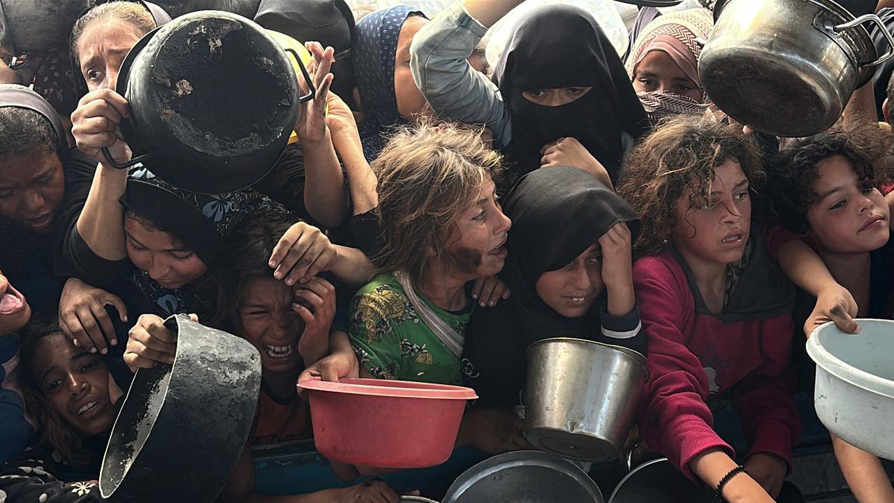 Hungernde Kinder drängen sich vor die Kamera und halten Schüsseln in der Hand