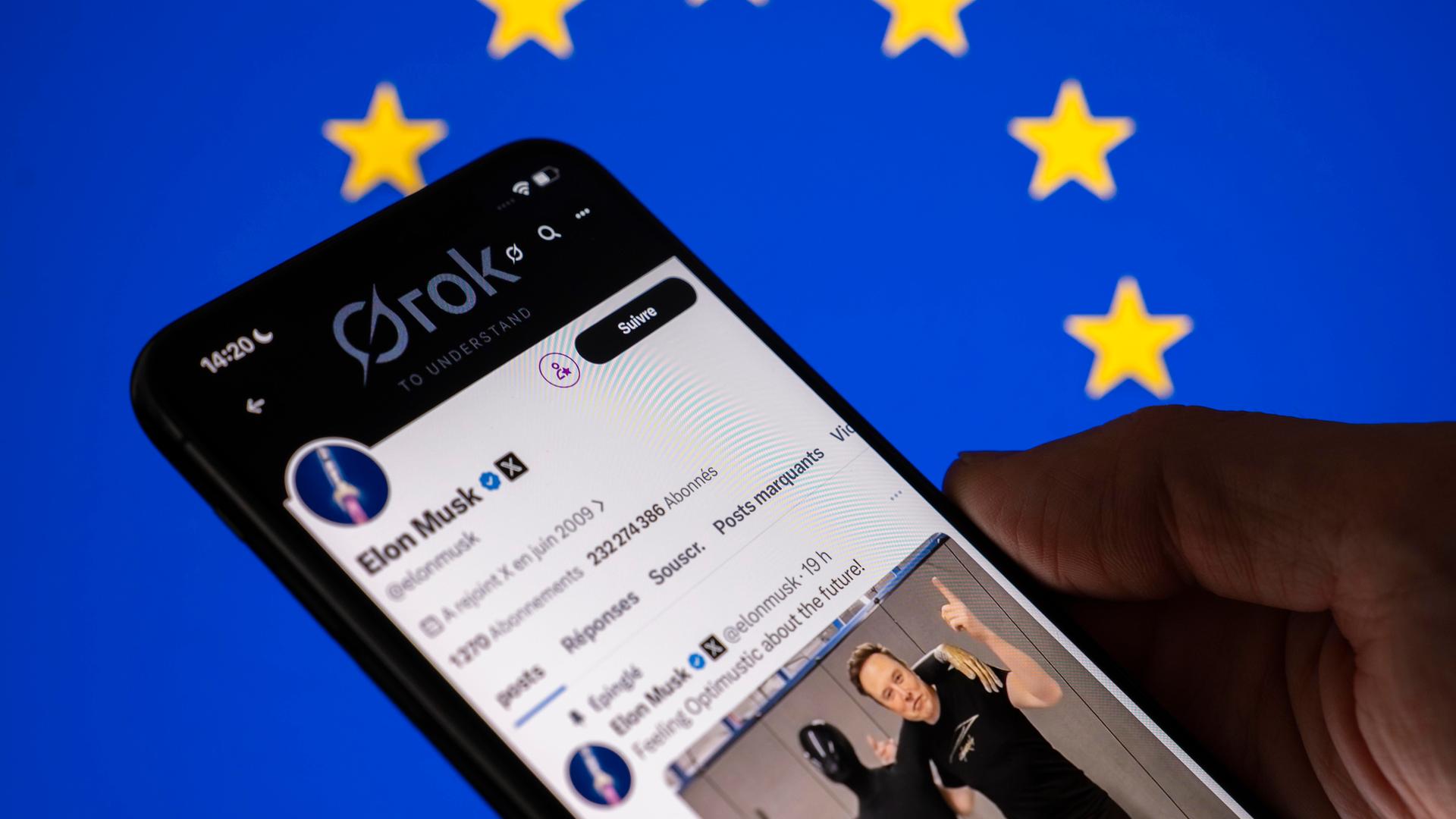 Eine Hand hält ein Mobiltelefon auf dessen Bildschirm der KI-Chatbot Grok der Plattform X zu sehen ist. 