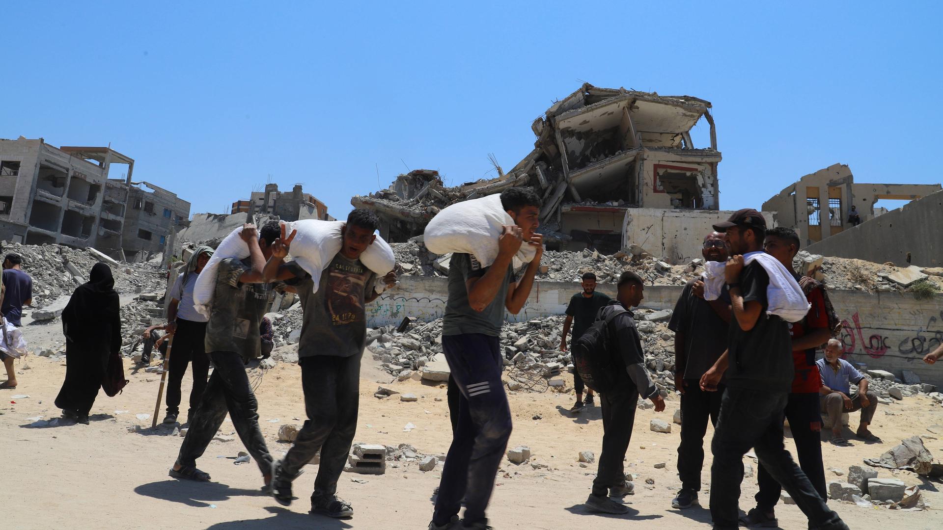 Einige Männer tragen Säcke in Jabalia im Gazastreifen. Im Hintergrund sind zerstörte Wohnhäuesr zu sehen. Einige Männer tragen Säcke in Jabalia im Gazastreifen. Im Hintergrund sind zerstörte Wohnhäuesr zu sehen.