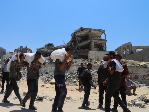 Einige Männer tragen Säcke in Jabalia im Gazastreifen. Im Hintergrund sind zerstörte Wohnhäuesr zu sehen. 