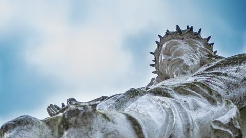 Blick nach oben zu einem steinernen Cruzifix. Jesus trägt eine Dornenkrone.