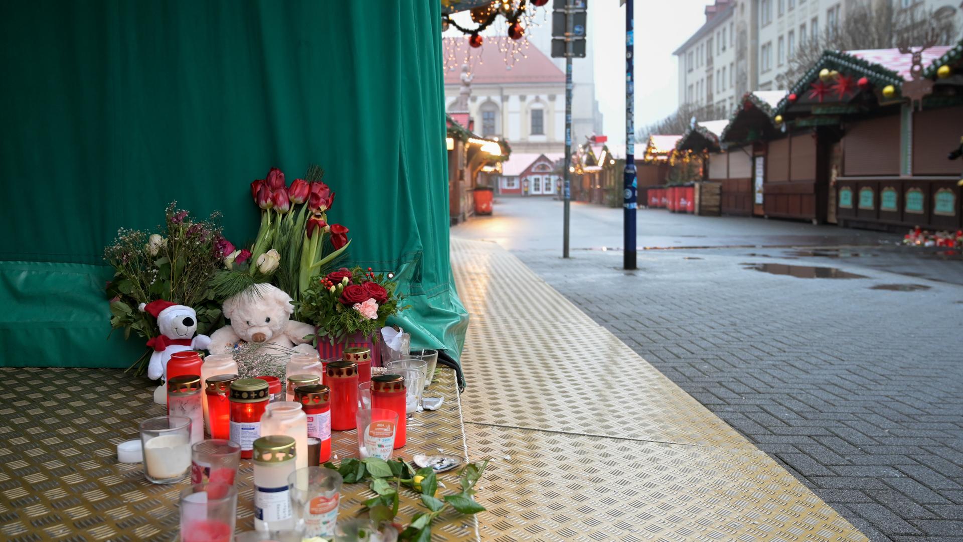 Kerzen, Kuscheltiere und Blumen stehen nach dem Anschlag in Magdeburg auf dem Boden an einem Stand auf dem Weihnachtsmarkt.