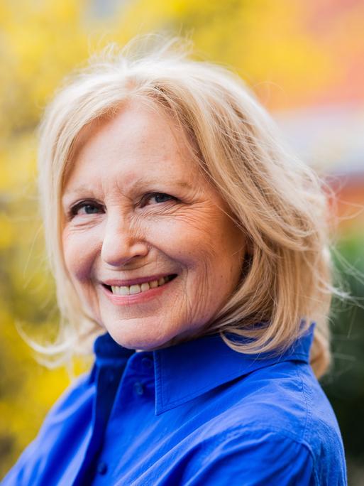 Die Schauspielerin und Kabarettistin Maren Kroymann trägt eine blaue Bluse und lächelt in die Kamera.