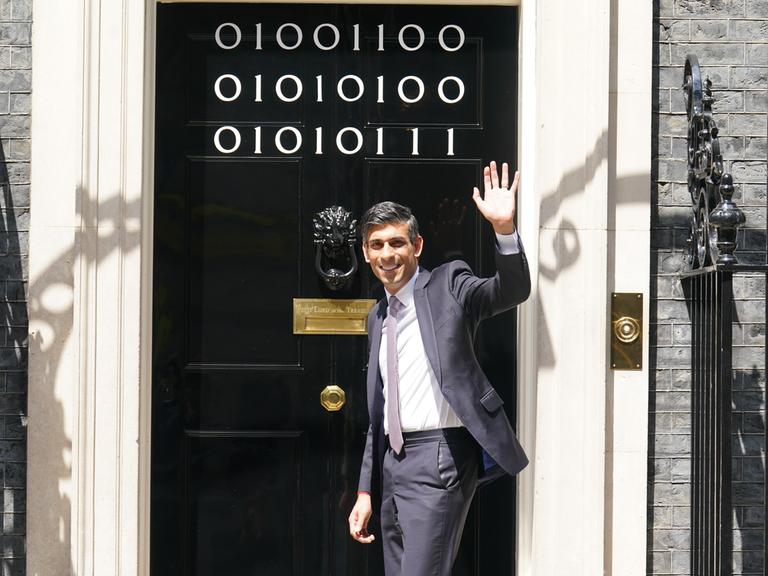 Prime Minister Rishi Sunak steht winkend vor der Tür von 10 Downing Street, auf der "London Tech Week" in Binärcode geschrieben steht.