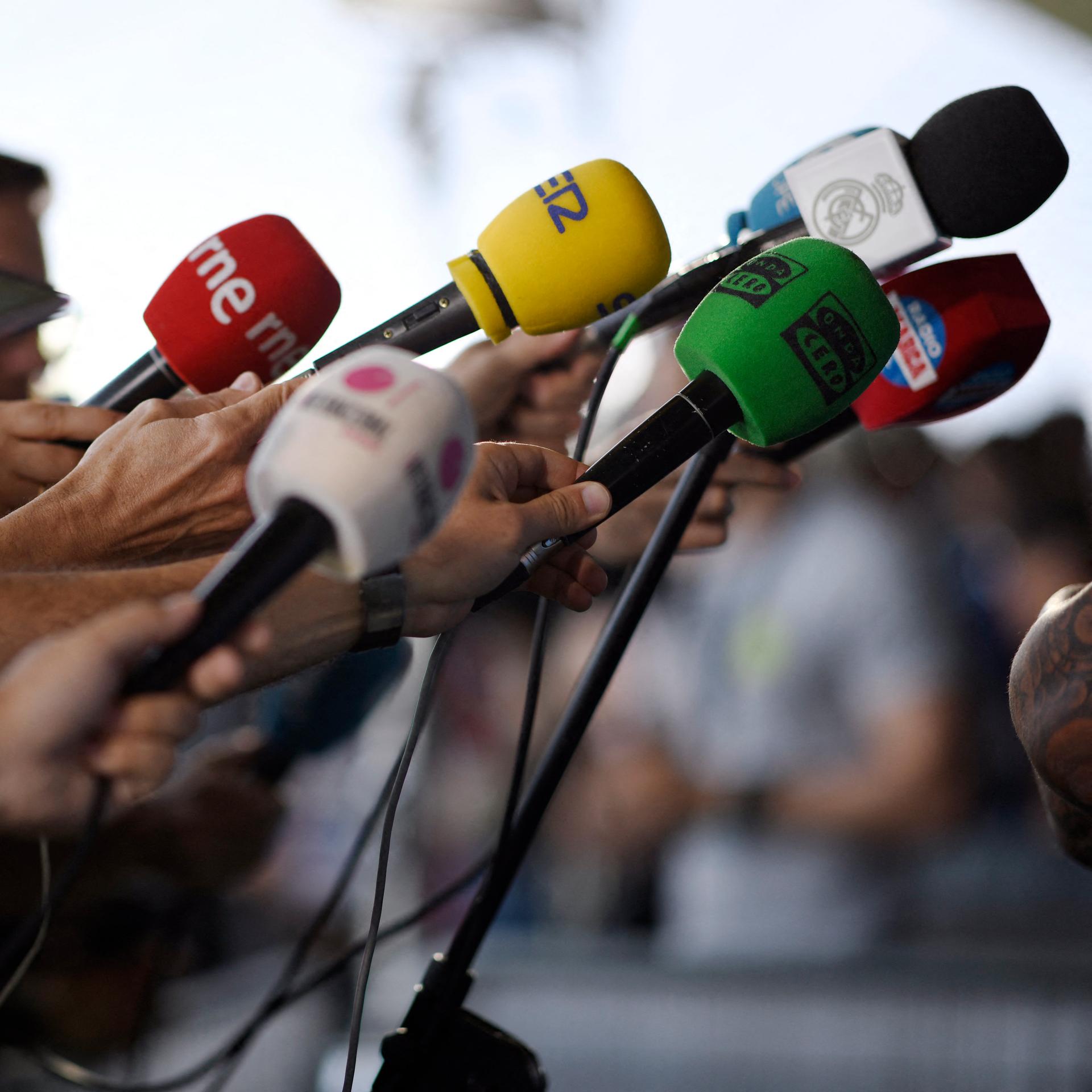 Journalisten halten ihre Mikrofone in Richtung eines Redners.