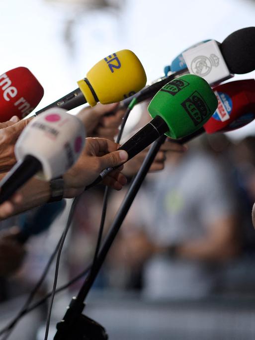 Journalisten halten ihre Mikrofone in Richtung eines Redners.