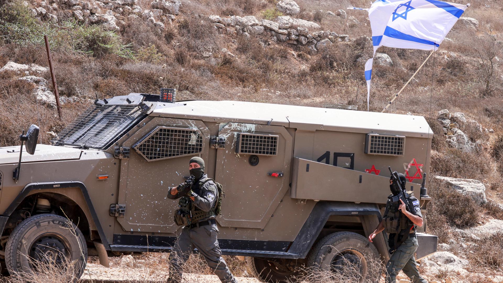 Ein israelischer Soldat läuft neben einem Panzerwagen im Westjordanland. An dem Fahrezeug ist die israelische Flagge. Ein israelischer Soldat läuft neben einem Panzerwagen im Westjordanland. An dem Fahrezeug ist die israelische Flagge.
