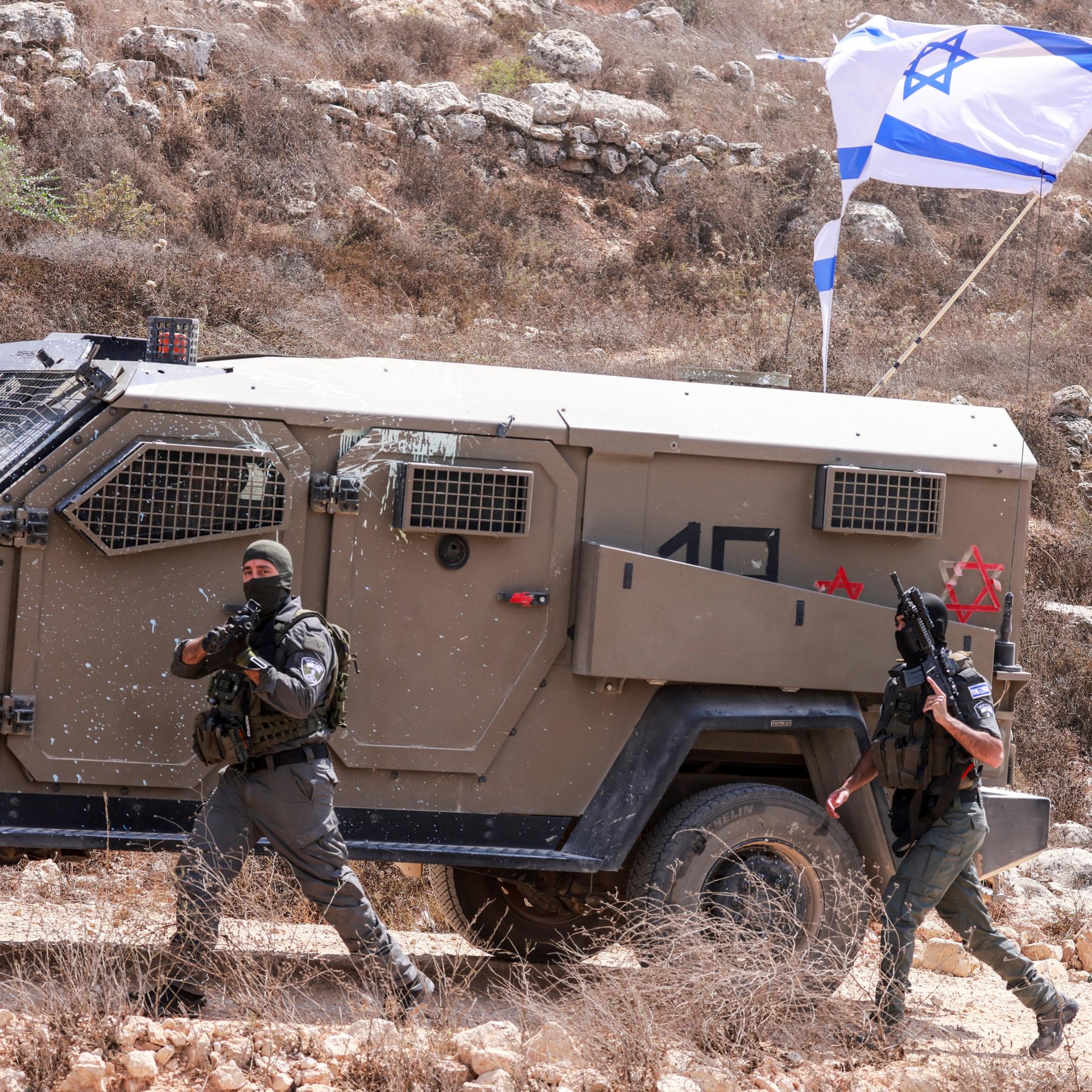 Ein israelischer Soldat läuft neben einem Panzerwagen im Westjordanland. An dem Fahrezeug ist die israelische Flagge.