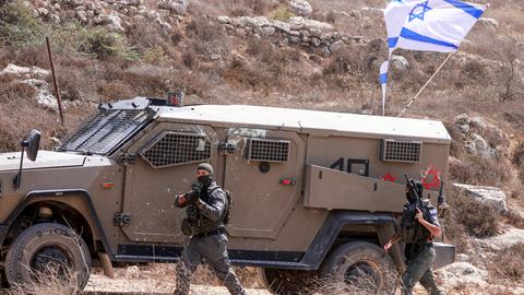 Ein israelischer Soldat läuft neben einem Panzerwagen im Westjordanland. An dem Fahrezeug ist die israelische Flagge.