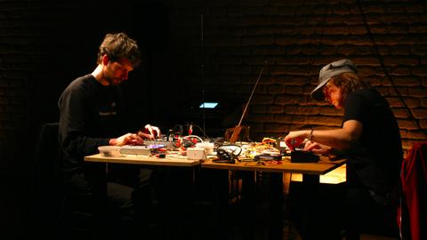 Zwei Bastler gegenüber am Tisch mit allerlei Radioapparaturen Zwei Bastler gegenüber am Tisch mit allerlei Radioapparaturen