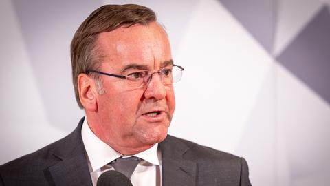 Pistorius steht vor einer Wand in verschiedenen Grautönen und sagte etwas. Sein Kopf ist zu Seite gedreht; er trägt Jackett und Krawatte.
