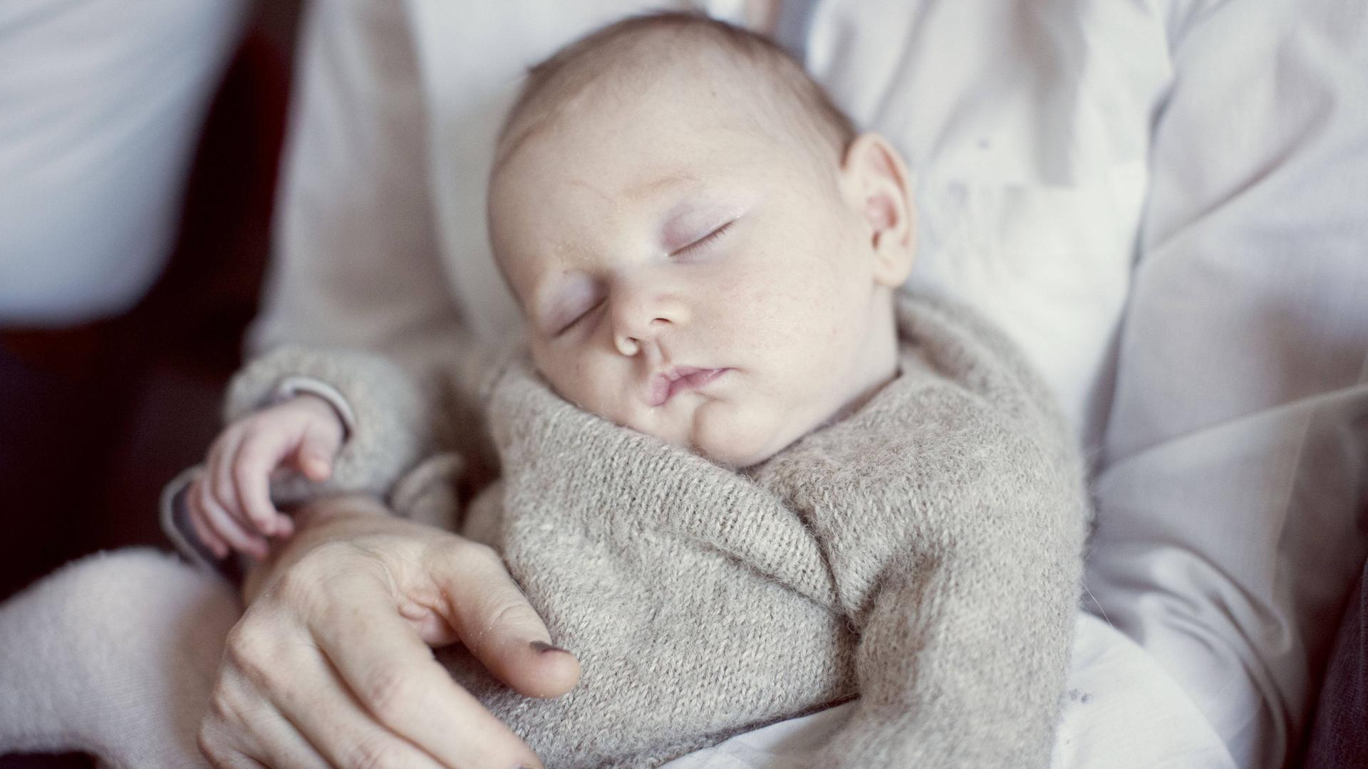 Ein neugeborenes Baby schläft auf dem Schoß seiner Mutter. Ein neugeborenes Baby schläft auf dem Schoß seiner Mutter.