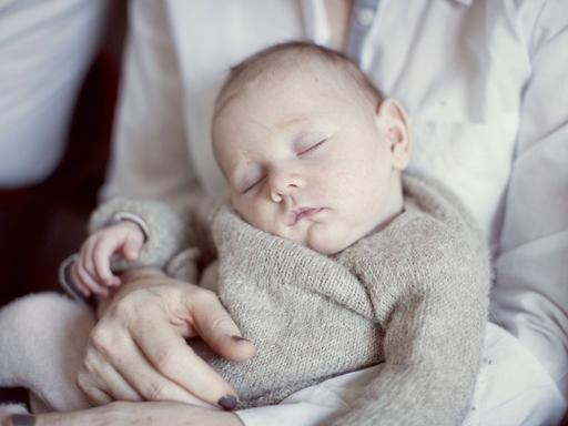 Ein neugeborenes Baby schläft auf dem Schoß seiner Mutter.