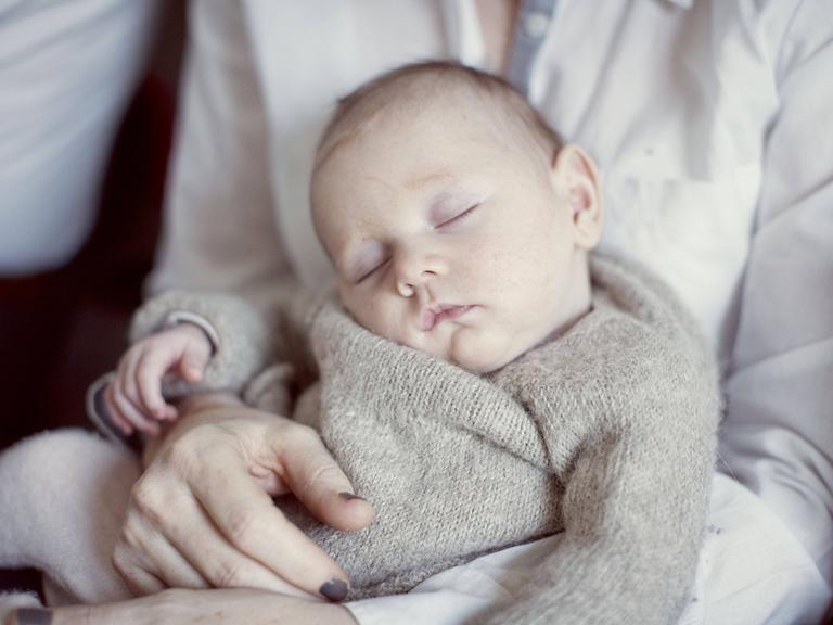 Ein neugeborenes Baby schläft auf dem Schoß seiner Mutter.