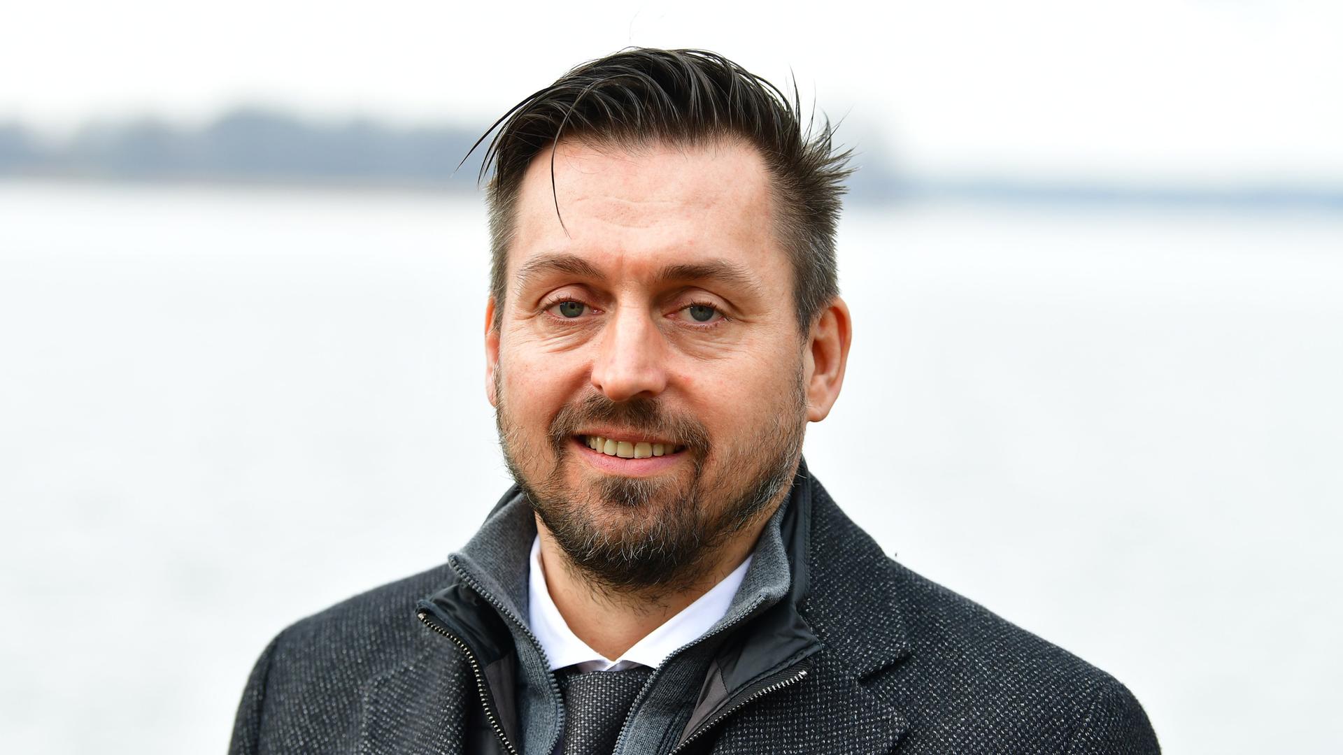 Ein Mann mit grauem Mantel und Jacket lächelt in die Kamera. Es ist Oliver Borchert, der Bürgermeister von Wandlitz.