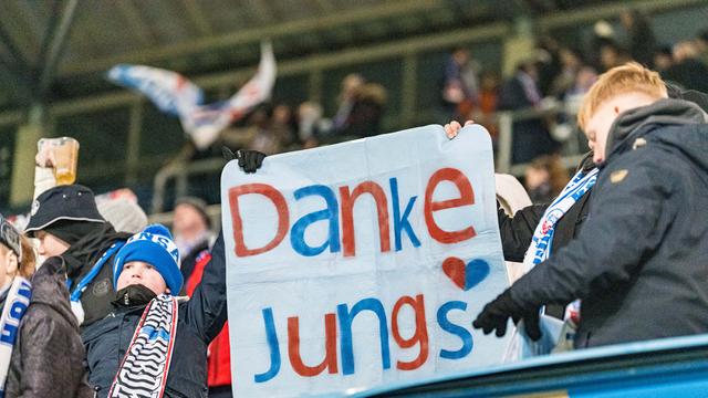 Zwei Fußballfans halten ein Schild im Stadion hoch mit der Aufschrift "Danke Jungs". 