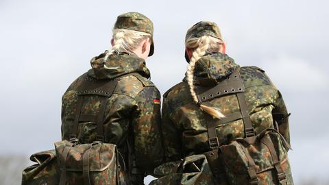 Das Foto zeigt Soldatinnen der Bundeswehr von der Hinterseite und in Tarnkleidung. Aus ihren Mützen hängt jeweils ein langer blonder Haarzopf heraus. 