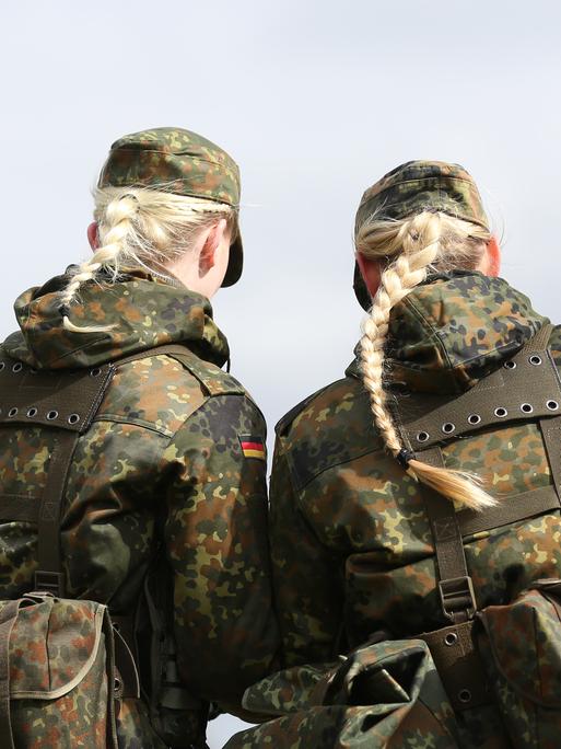 Das Foto zeigt Soldatinnen der Bundeswehr von der Hinterseite und in Tarnkleidung. Aus ihren Mützen hängt jeweils ein langer blonder Haarzopf heraus. 