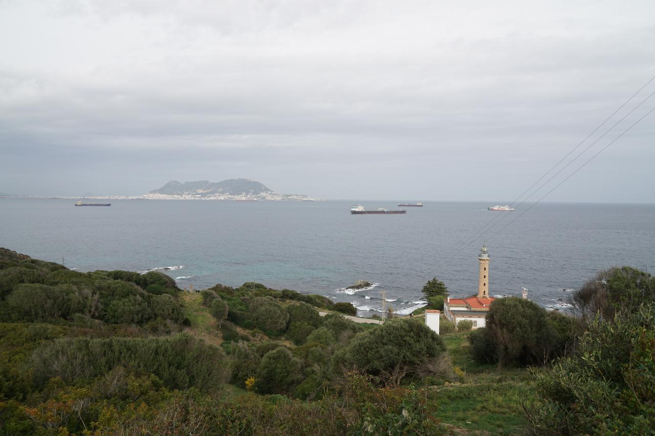 Blick von oben von der grün bewachsenen Küste auf das Meer mit mehreren Schiffen. In der Ferne ein hoher Felsen.