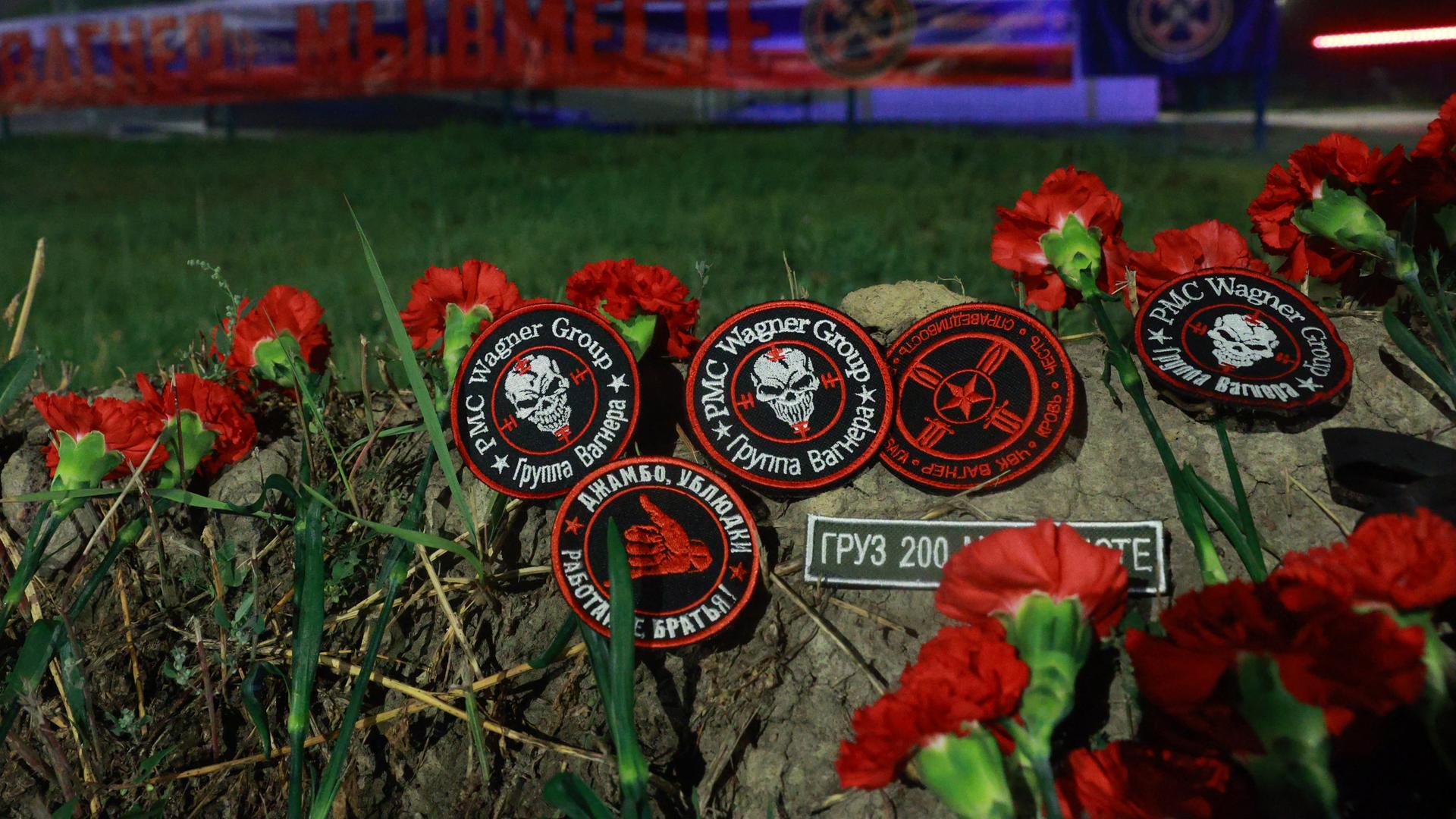 Rote Blumen auf Aufnäher mit dem Wagner-Logo liegen auf einer improvisierten Gedenkstätte vor dem "PMC Wagner Centre" in St. Petersburg.