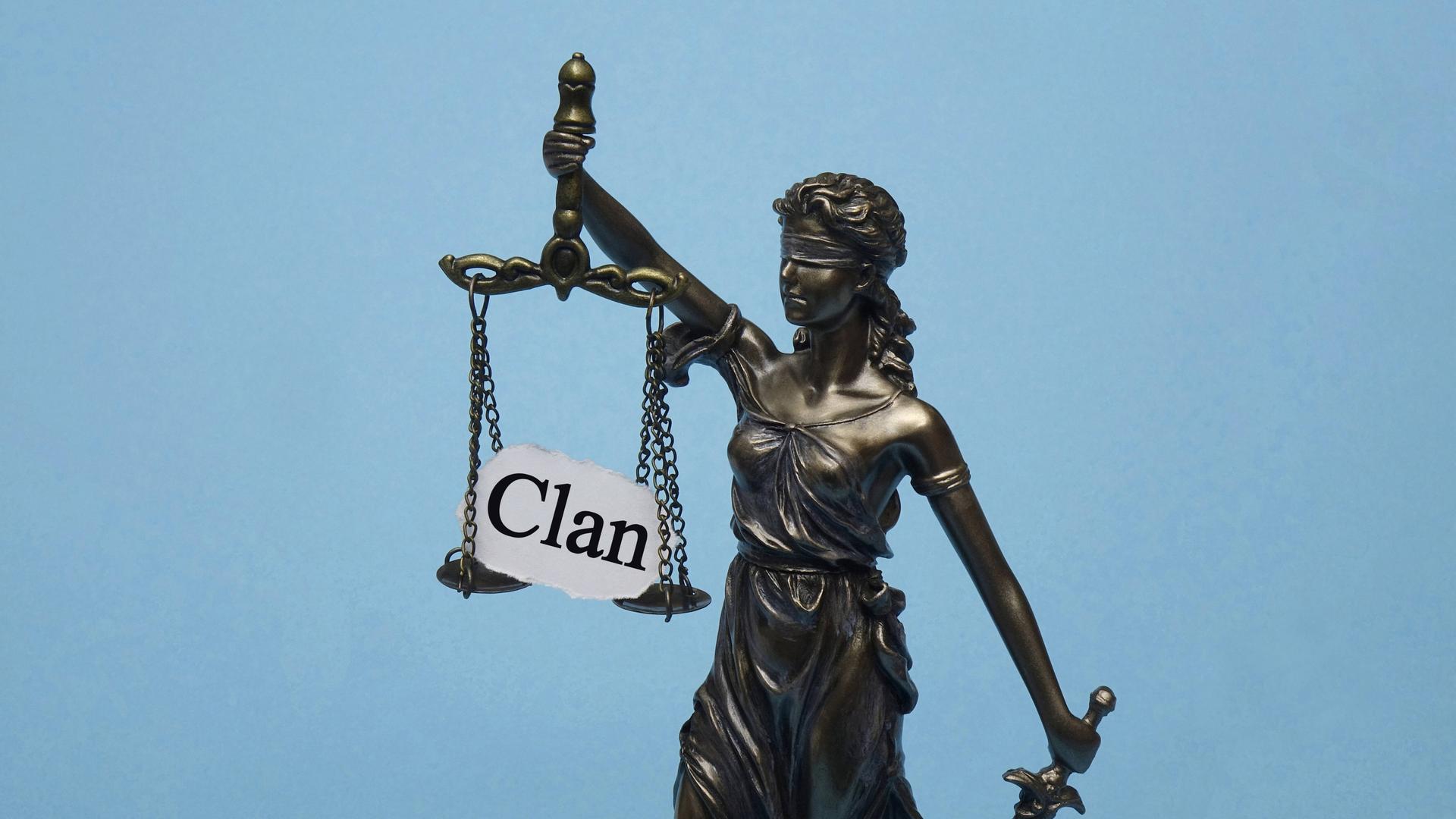 Justitia hält ihre Waage, auf der ein Papier liegt mit dem Wort "Clan" 