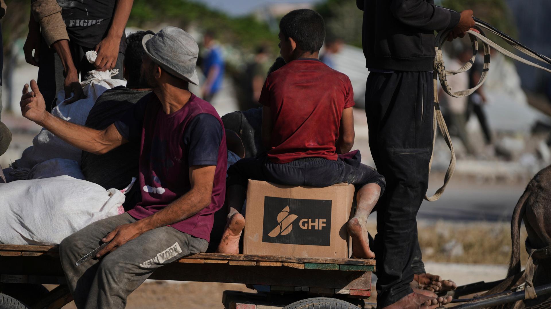 Mehrere Menschen auf einem Eselswagen mit einem Paket der Gaza Humanitarian Foundation, kurz GHM Mehrere Menschen auf einem Eselswagen mit einem Paket der Gaza Humanitarian Foundation, kurz GHM