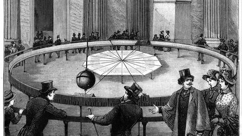 Eine alte Aufnahme zeigt mehrere Menschen, die von der Decke hängendes Pendel beobachten.